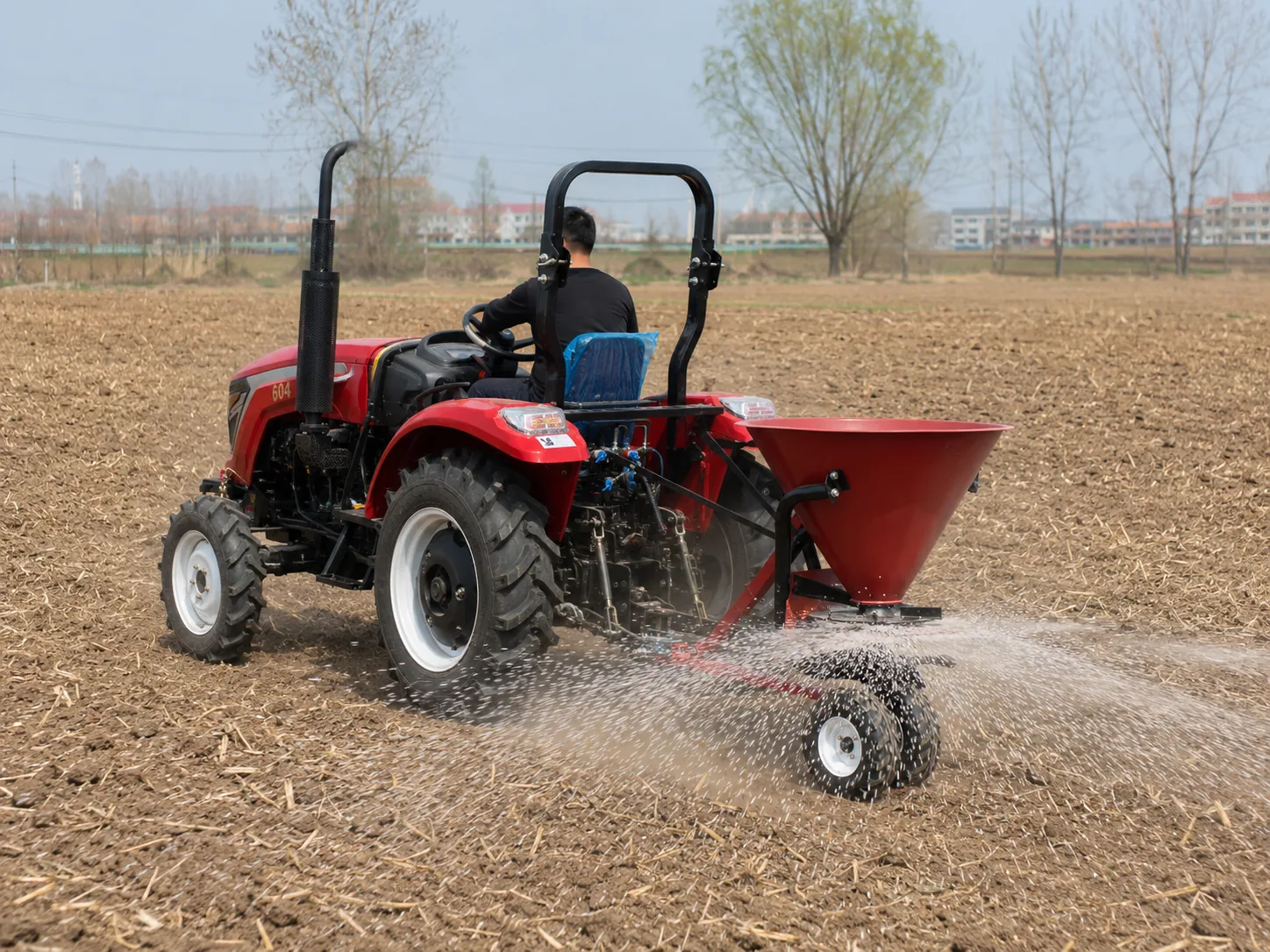 Esparcidor de fertilizante montado en un tractor que esparce fertilizante granulado por las tierras de cultivo