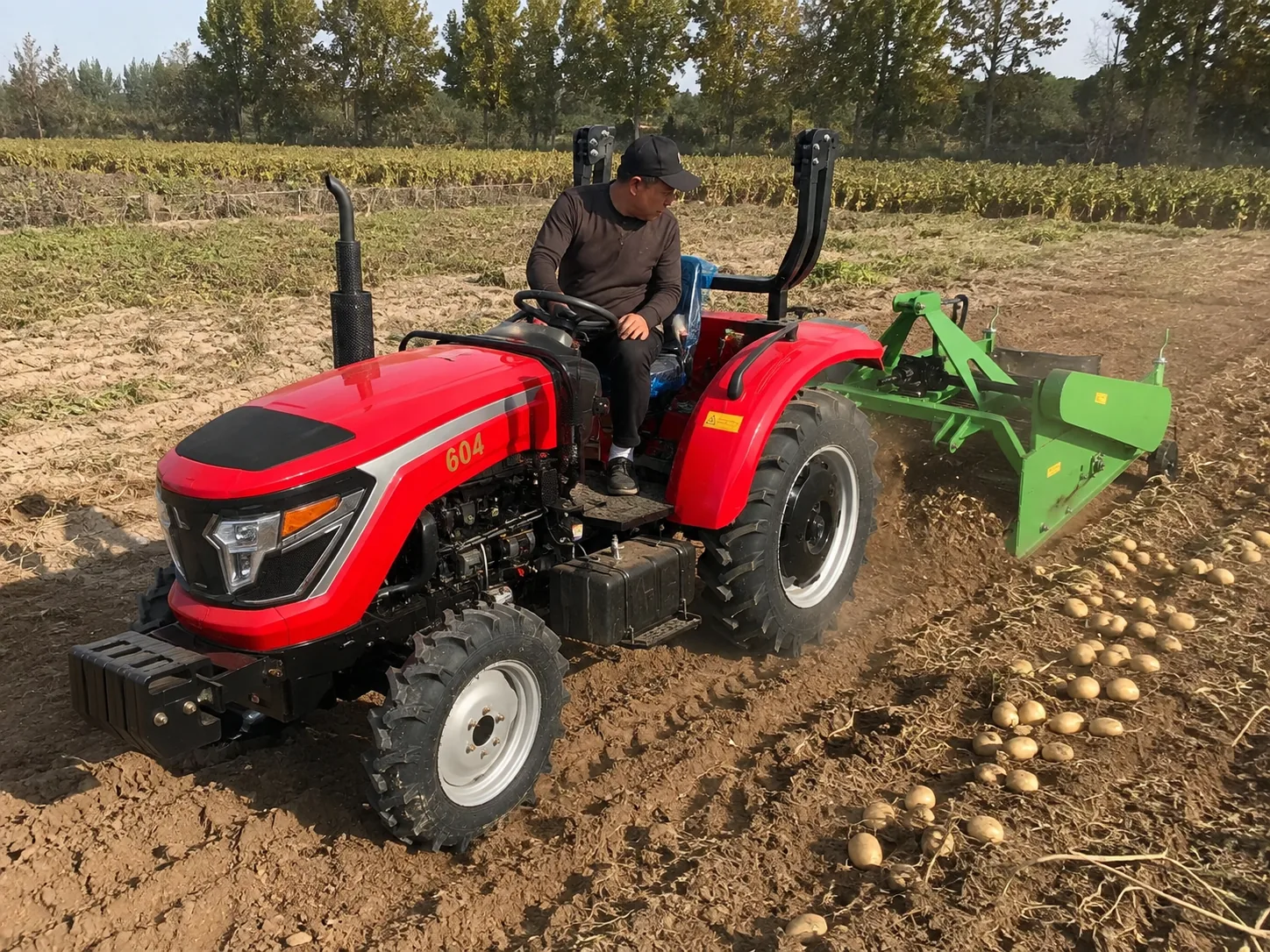 Tractor rojo con tracción a las cuatro ruedas que utiliza una cosechadora de patatas montada en la parte trasera en un campo